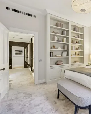 Calm bedroom with upholstered bed, built-in bookshelves, bedside lamps, and a soft bench.