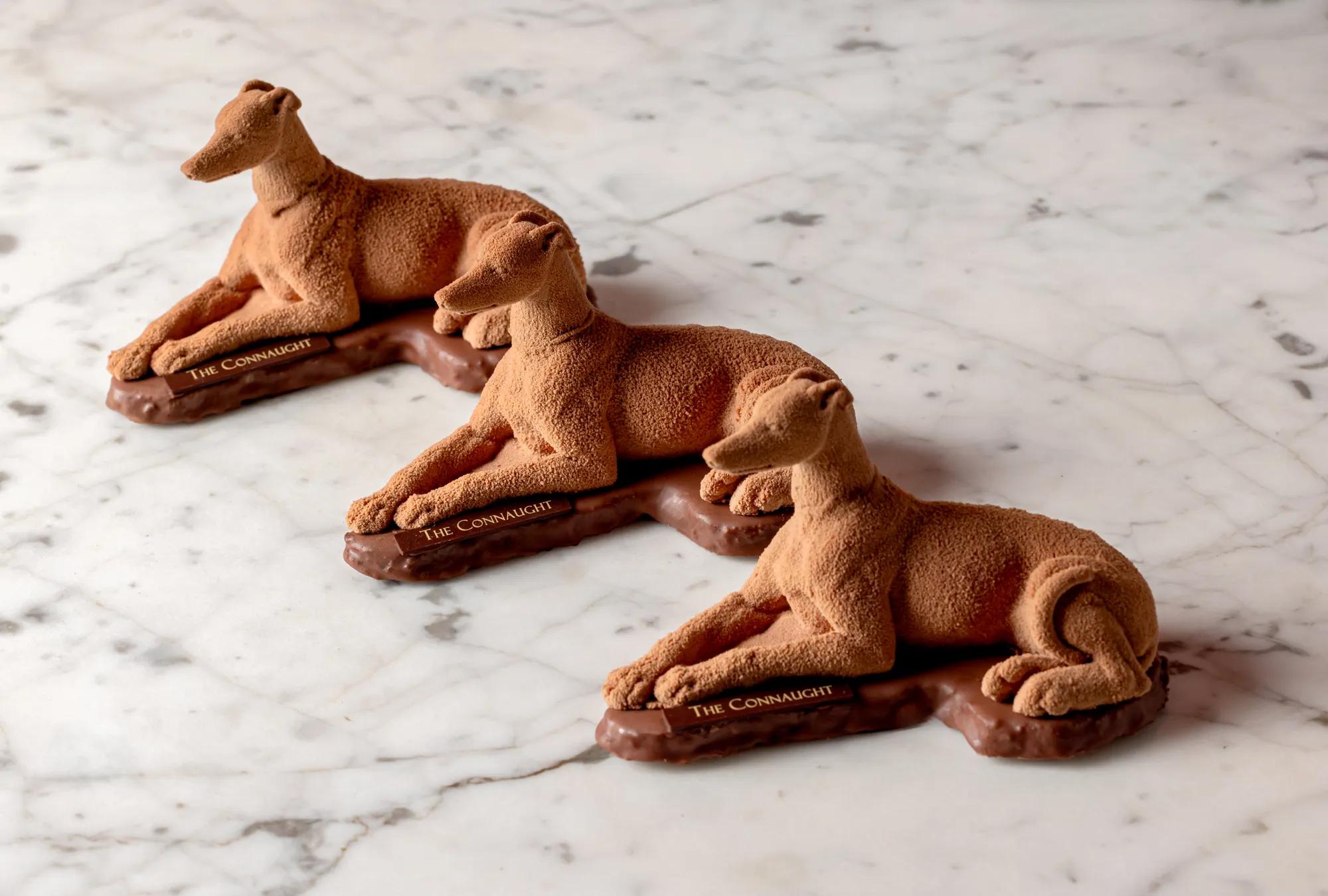 Three chocolate sculptures shaped like reclining greyhound dogs displayed on a marble surface.