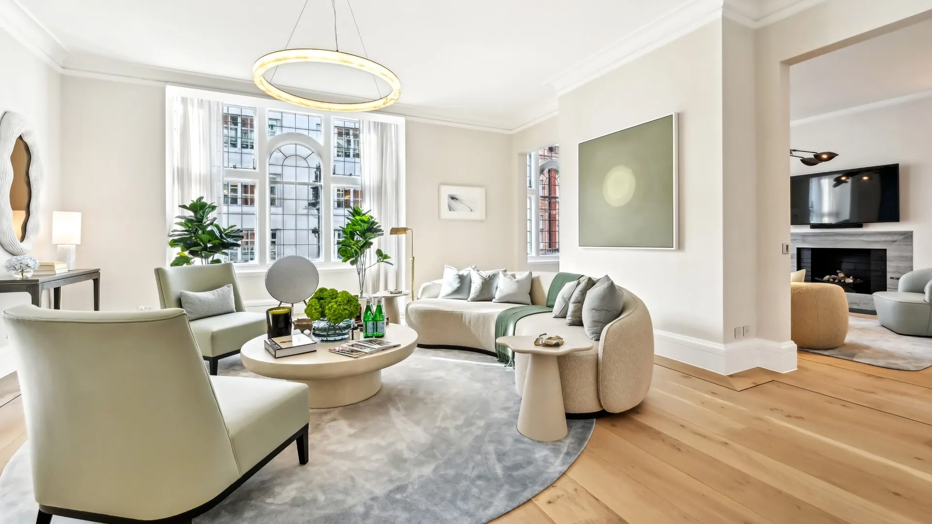 Bright living room with curved sofa, armchairs, round coffee table, and large arched window.