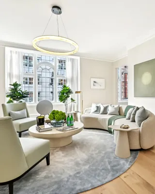 Bright living room with curved sofa, armchairs, round coffee table, and large arched window.