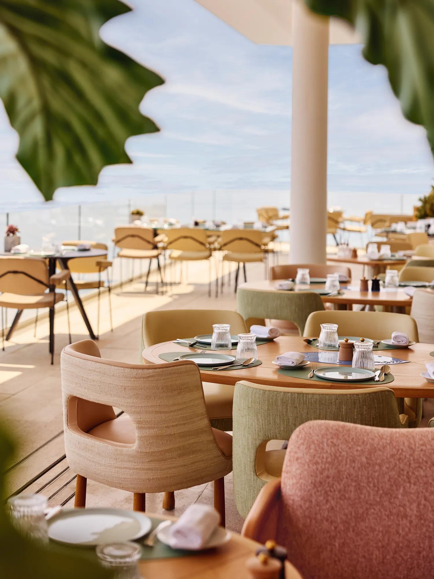 Terrasse ensoleillée de restaurant avec chaises pastel et tables dressées face à la mer