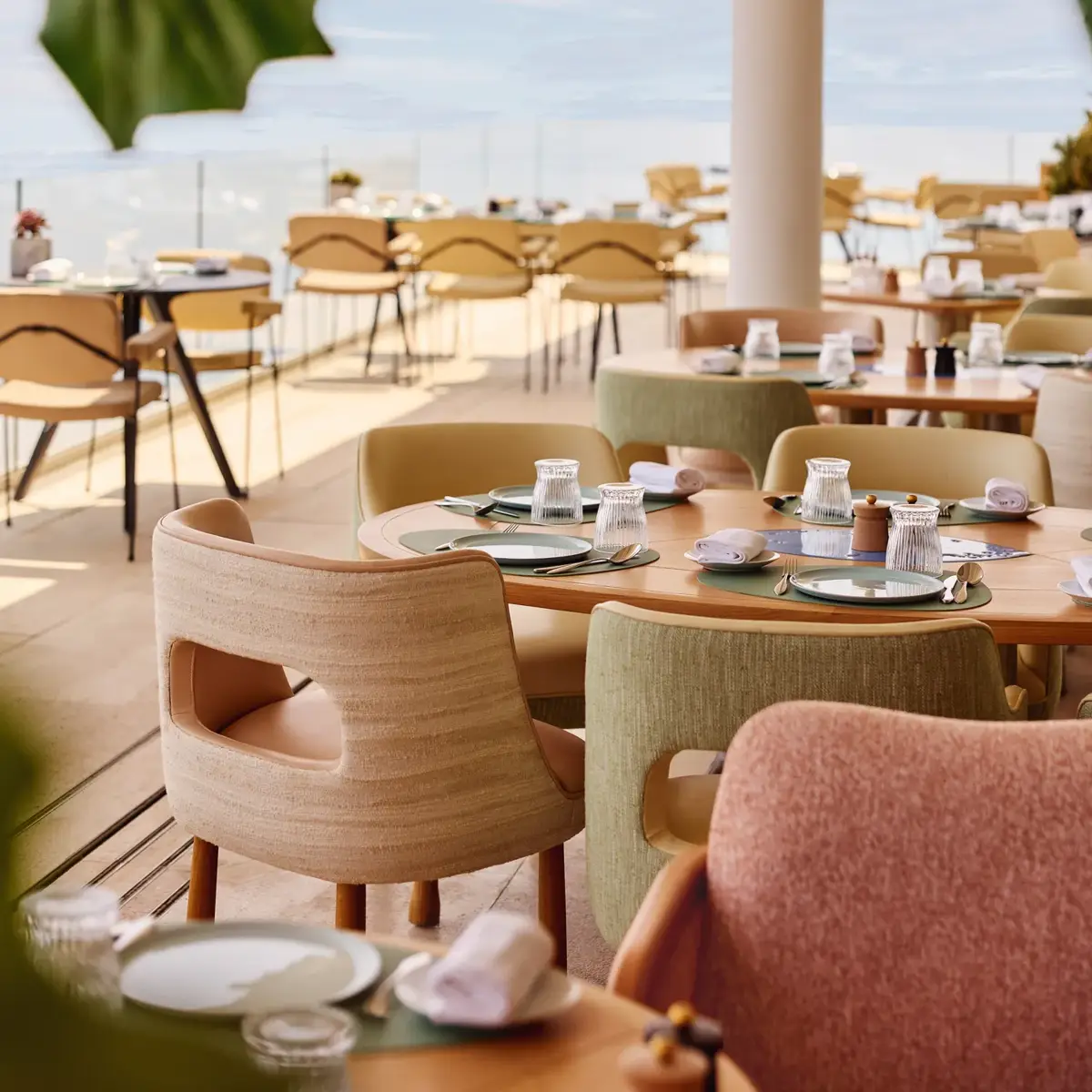 Terrasse ensoleillée de restaurant avec chaises pastel et tables dressées face à la mer