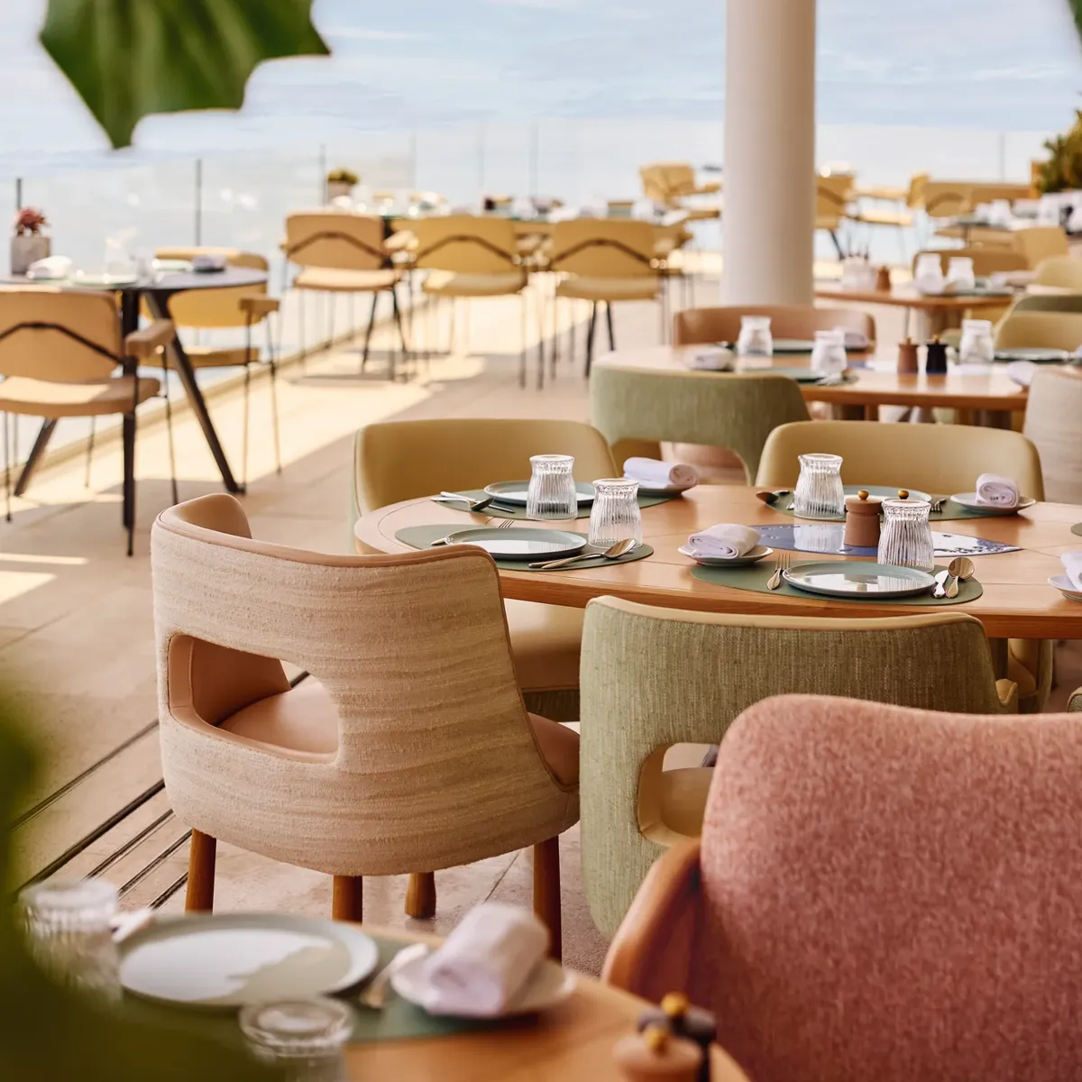 Sunny outdoor restaurant terrace with pastel chairs and set tables overlooking the sea
