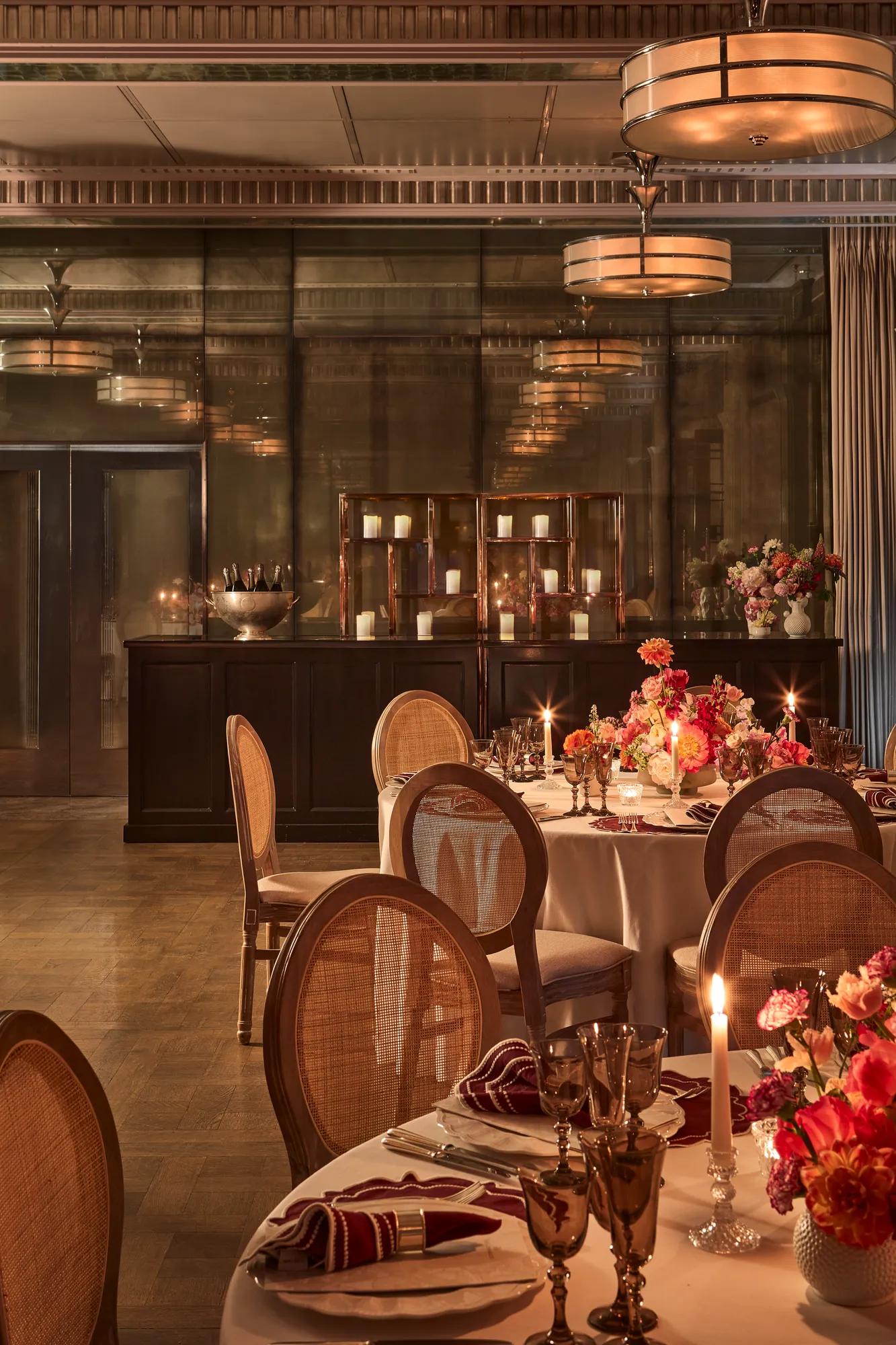 Elegant dining room with round tables set with flowers and candles, surrounded by cane-back chairs under warm ambient lighting.