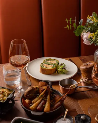 Salmon Wellington served with greens, roast vegetables, sides, and wine on a warmly lit wooden dining table.