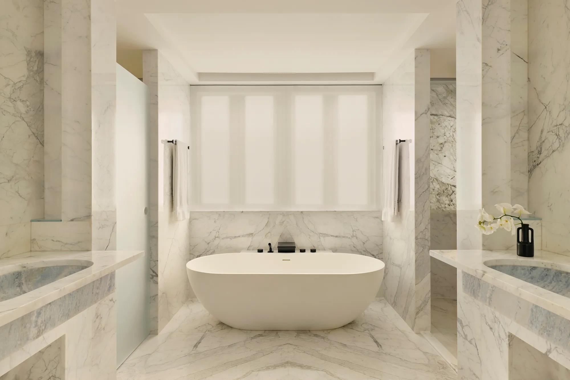 Luxurious marble bathroom with freestanding oval tub, double sinks, and soft natural light.