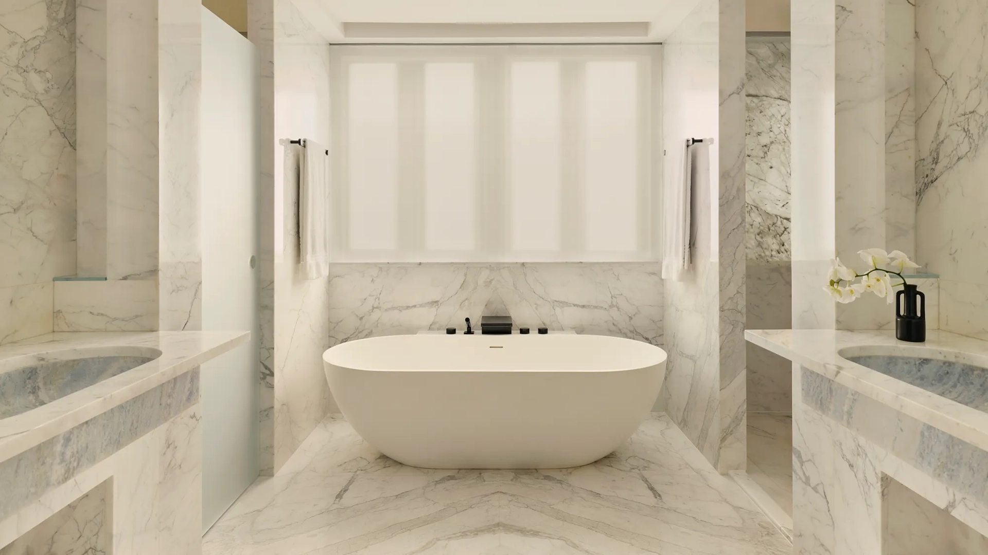 Luxurious marble bathroom with freestanding oval tub, double sinks, and soft natural light.