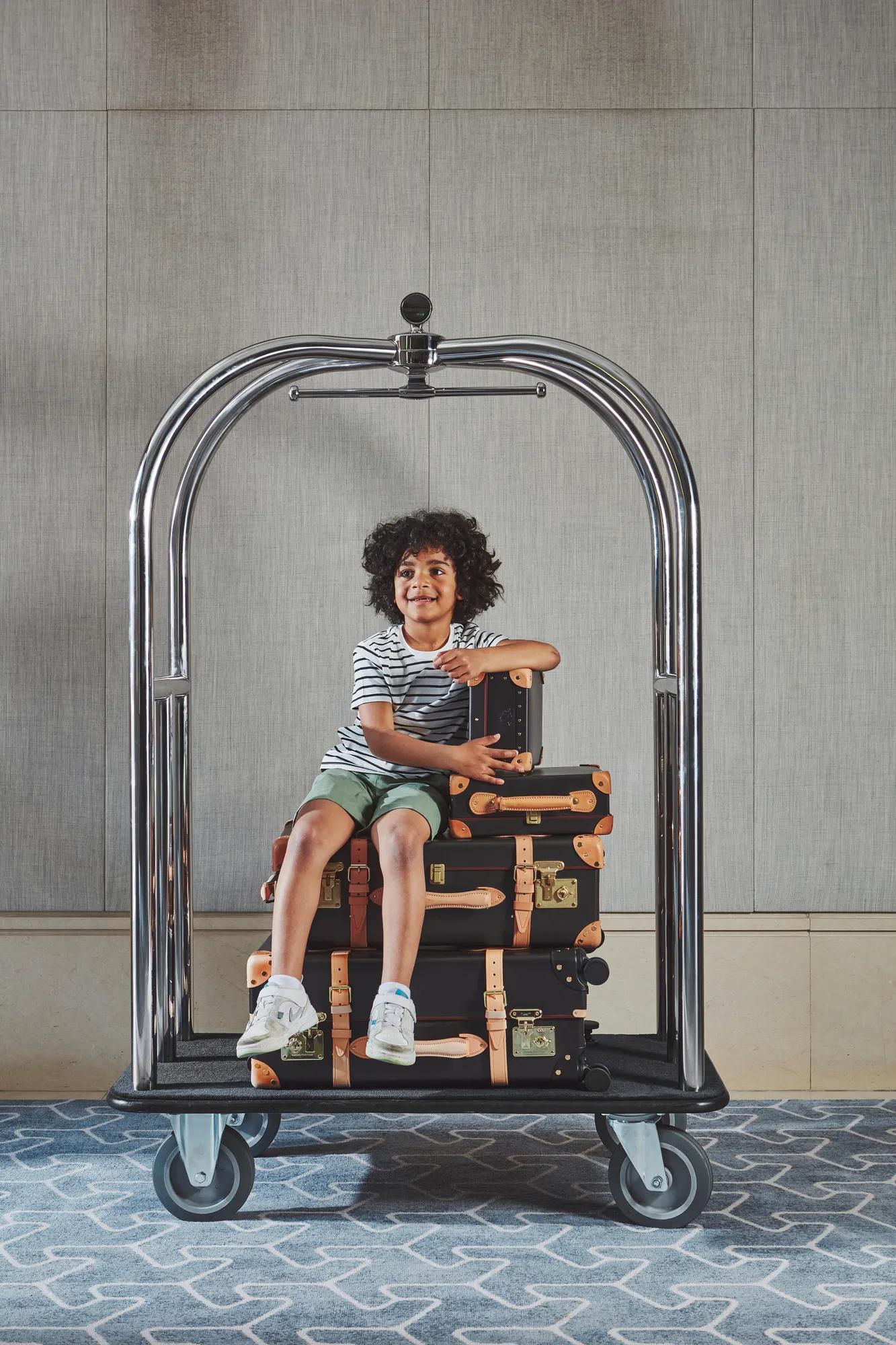 Child sitting on a luggage trolley, being pushed along in a playful, travel‑ready setting.