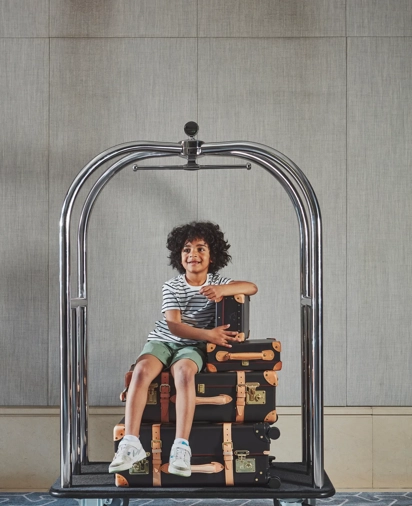 Child sitting on a luggage trolley, being pushed along in a playful, travel‑ready setting.