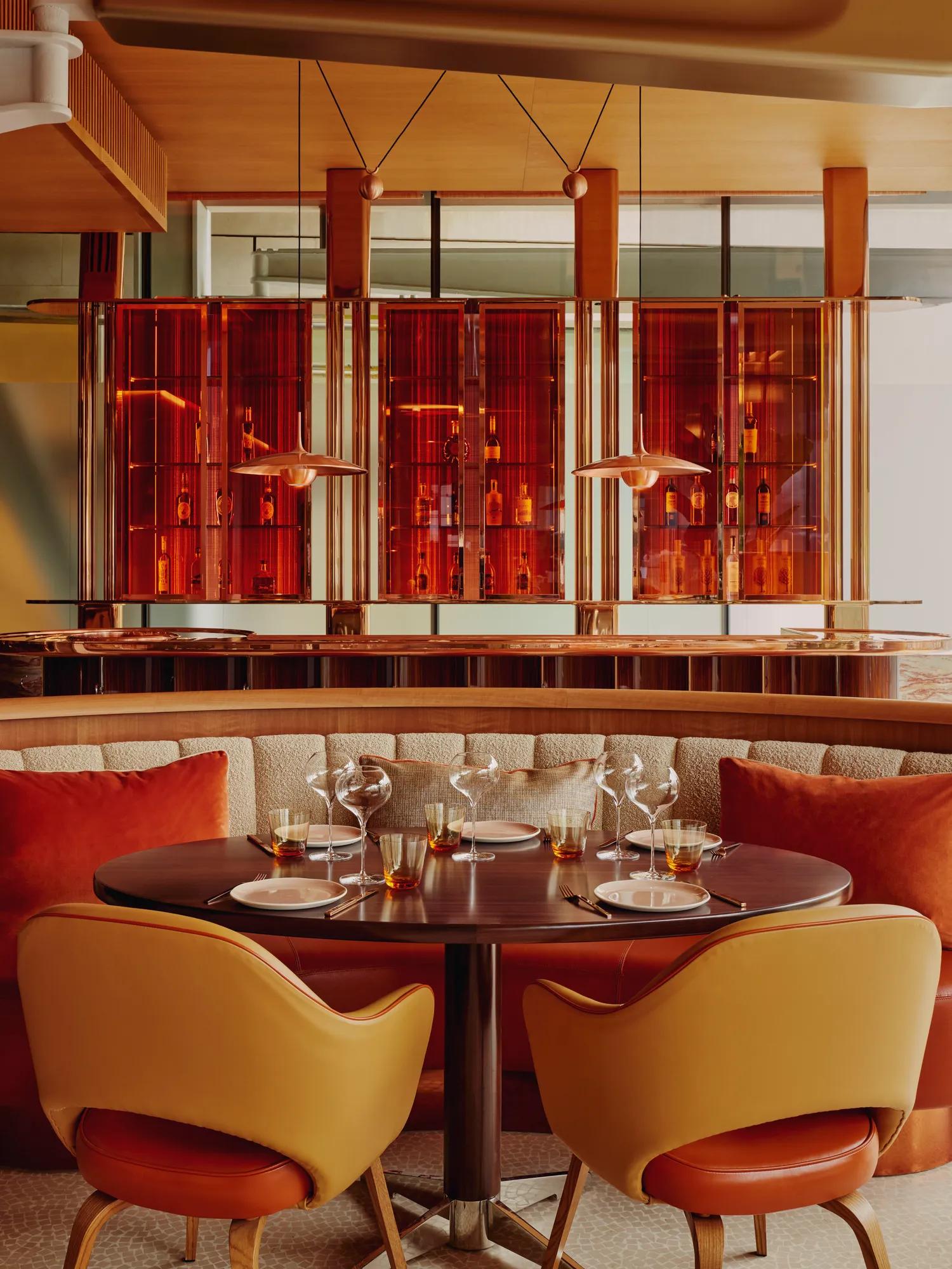 Elegant round dining table with amber glasses, cushioned seating, and glowing amber bar backdrop.