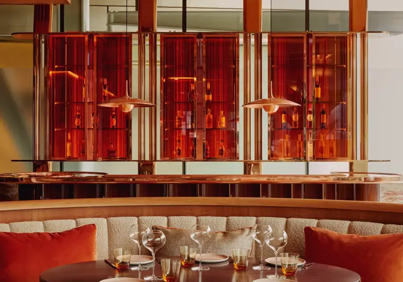 Elegant round dining table with amber glasses, cushioned seating, and glowing amber bar backdrop.