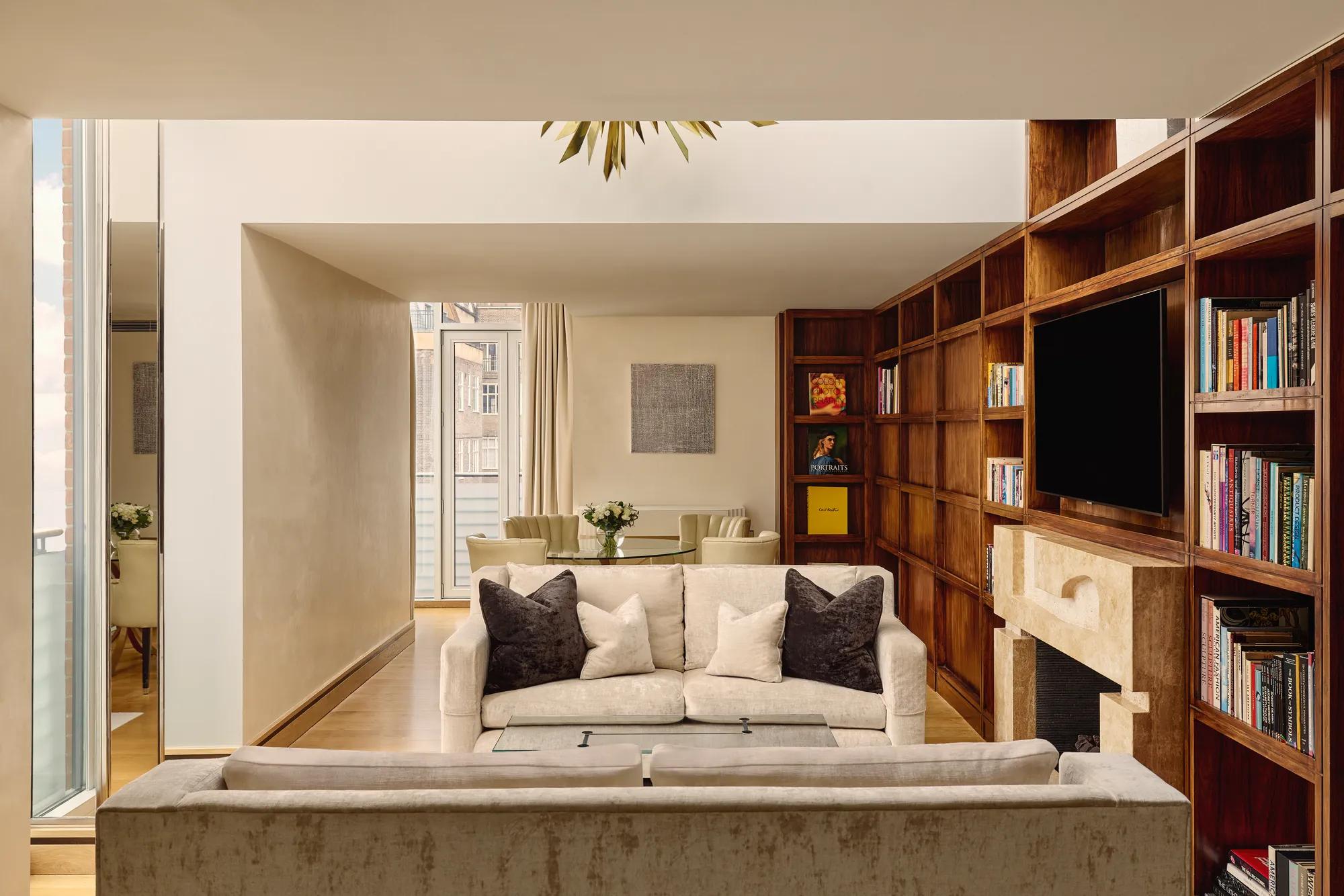 Spacious suite with cream sofas, wood bookcase wall, fireplace and dining table near balcony.