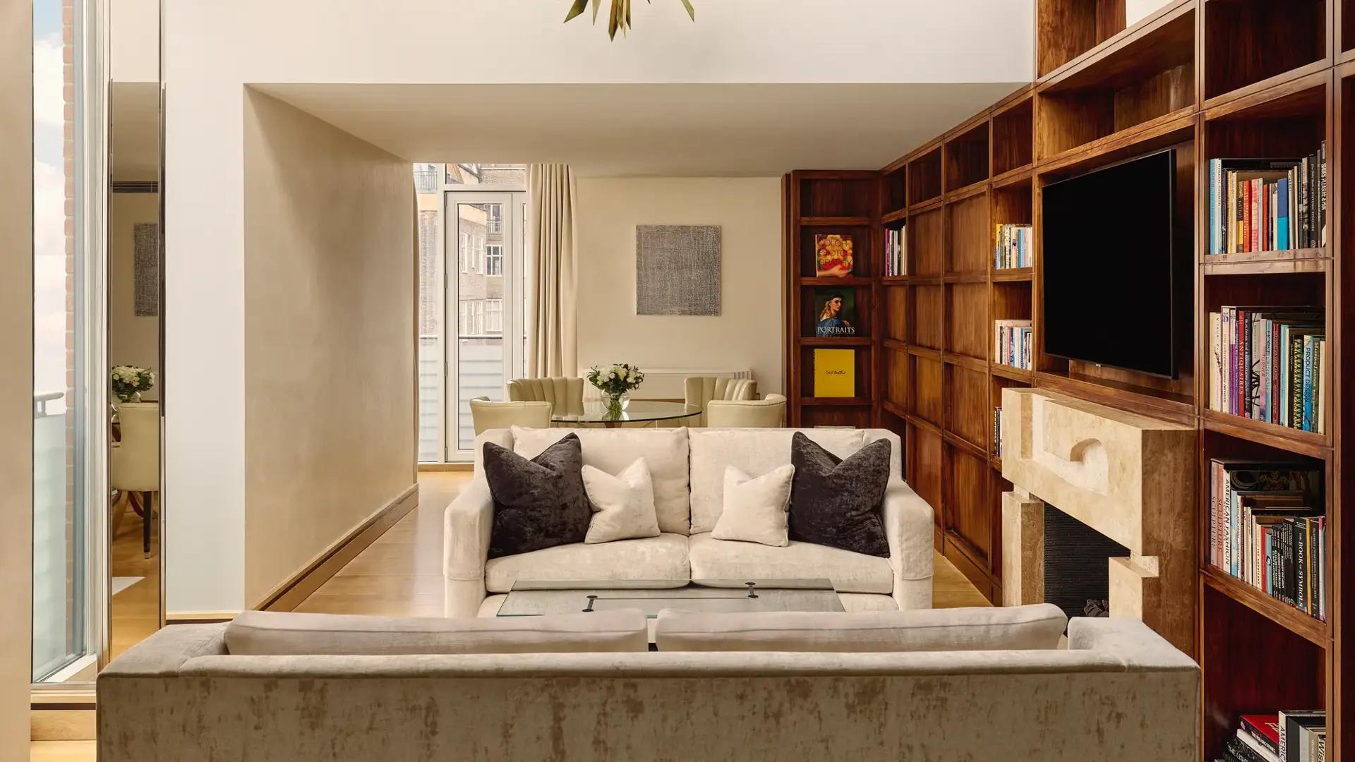 Spacious suite with cream sofas, wood bookcase wall, fireplace and dining table near balcony.