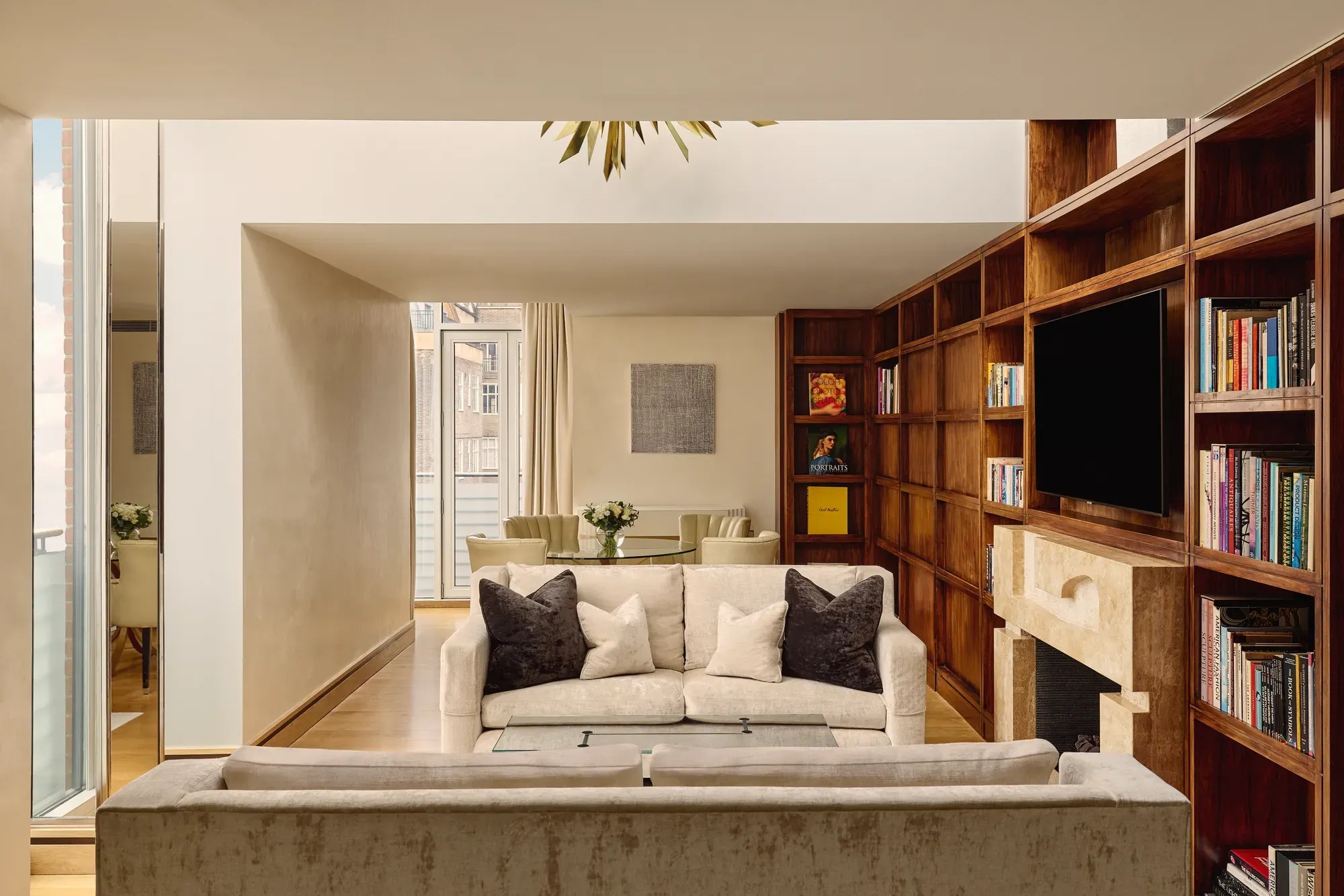 Spacious suite with cream sofas, wood bookcase wall, fireplace and dining table near balcony.