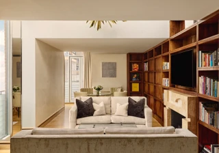 Spacious suite with cream sofas, wood bookcase wall, fireplace and dining table near balcony.