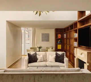 Spacious suite with cream sofas, wood bookcase wall, fireplace and dining table near balcony.