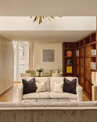 Spacious suite with cream sofas, wood bookcase wall, fireplace and dining table near balcony.