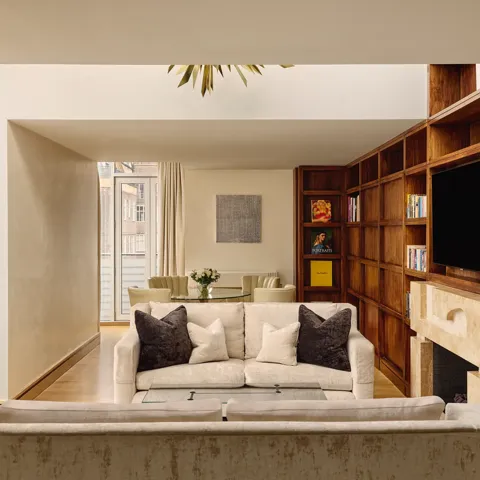 Spacious suite with cream sofas, wood bookcase wall, fireplace and dining table near balcony.