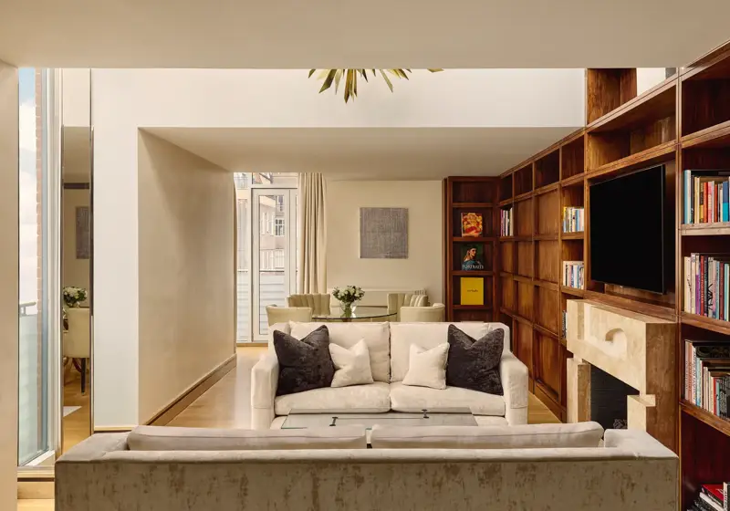 Spacious suite with cream sofas, wood bookcase wall, fireplace and dining table near balcony.