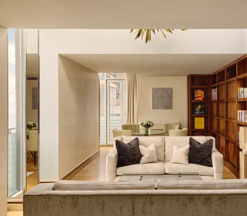 Spacious suite with cream sofas, wood bookcase wall, fireplace and dining table near balcony.