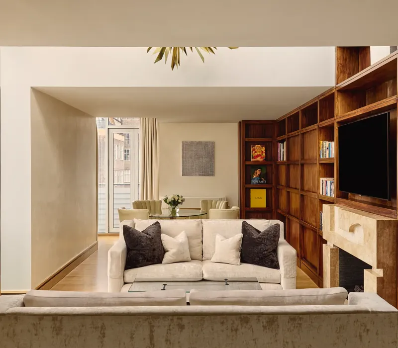 Spacious suite with cream sofas, wood bookcase wall, fireplace and dining table near balcony.