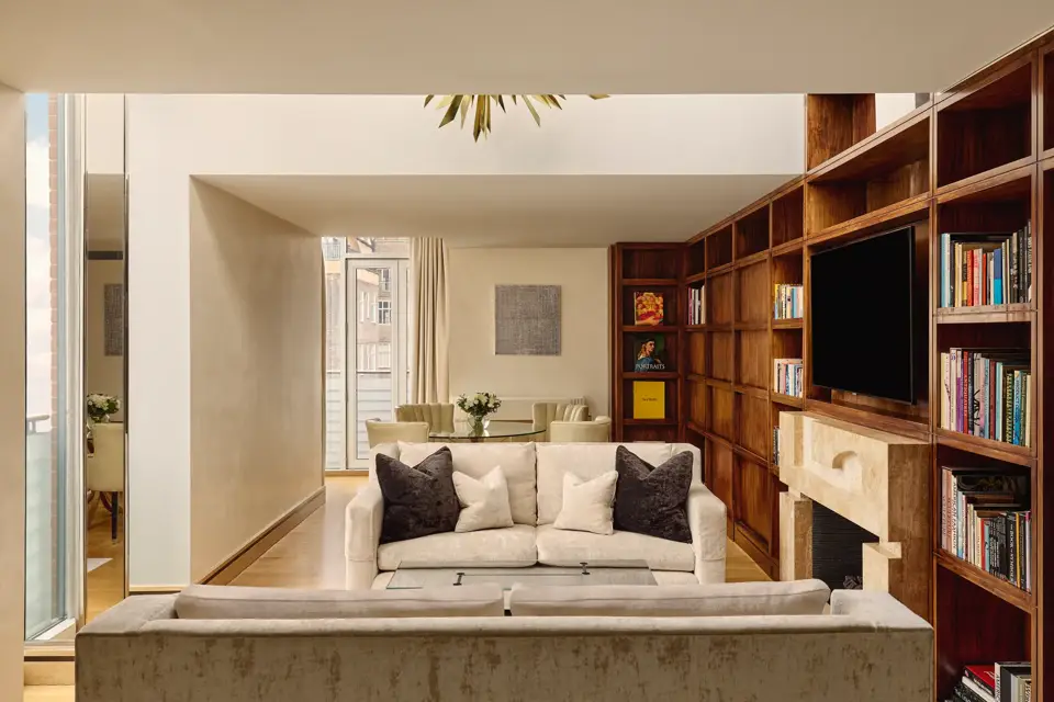 Spacious suite with cream sofas, wood bookcase wall, fireplace and dining table near balcony.