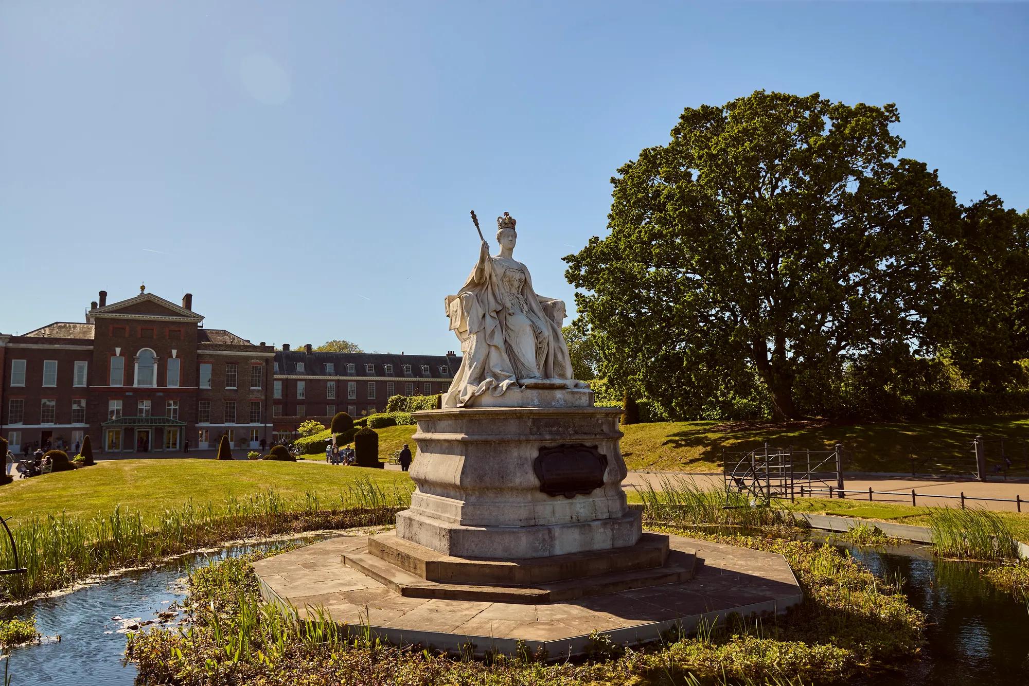 Statue in front of a historic building, surrounded by landscaped gardens and a reflecting pool.