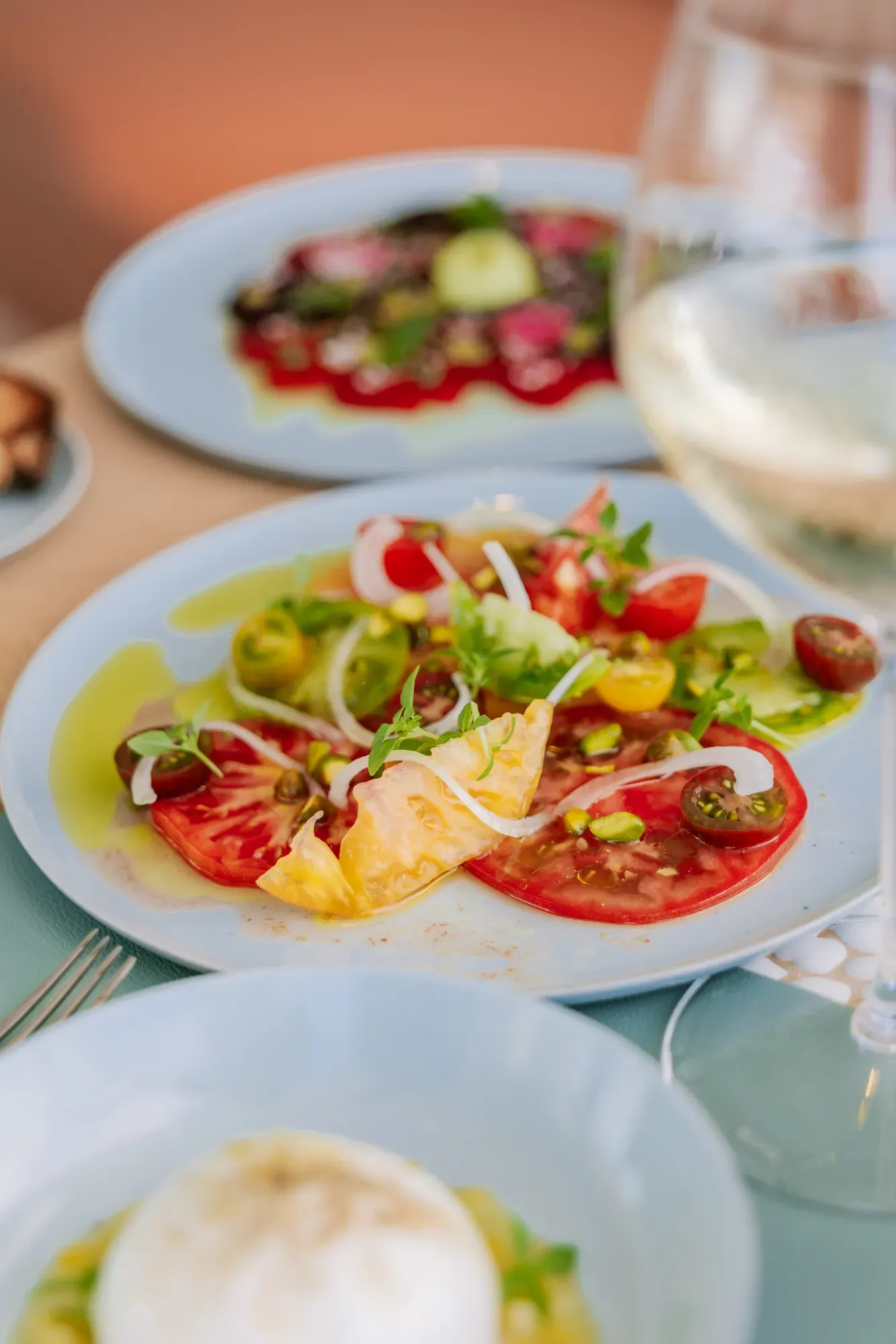 Assiette de salade de tomates anciennes avec oignons, roquette et huile d’olive, servie dans un plat bleu clair