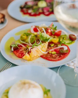 Assiette de salade de tomates anciennes avec oignons, roquette et huile d’olive, servie dans un plat bleu clair