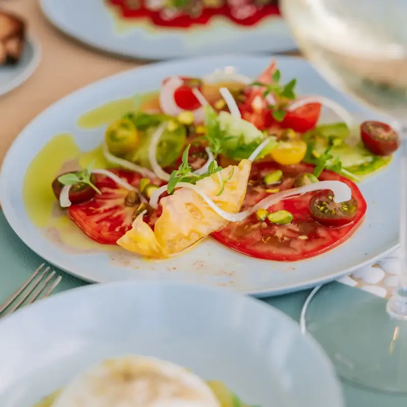 Assiette de salade de tomates anciennes avec oignons, roquette et huile d’olive, servie dans un plat bleu clair