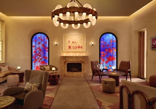 Lounge with fireplace, large circular chandelier, and two blue stained-glass windows with red accents.