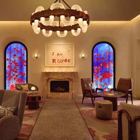 Lounge with fireplace, large circular chandelier, and two blue stained-glass windows with red accents.