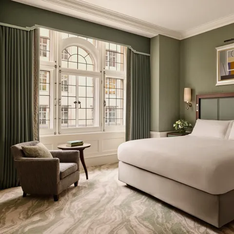 Elegant bedroom with king bed, green walls, armchair, and large arched window.