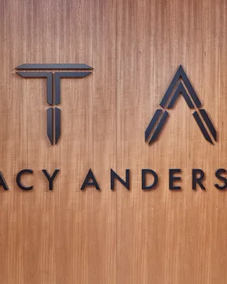 Tracy Anderson logo in black lettering and monogram on a warm wood-paneled wall.