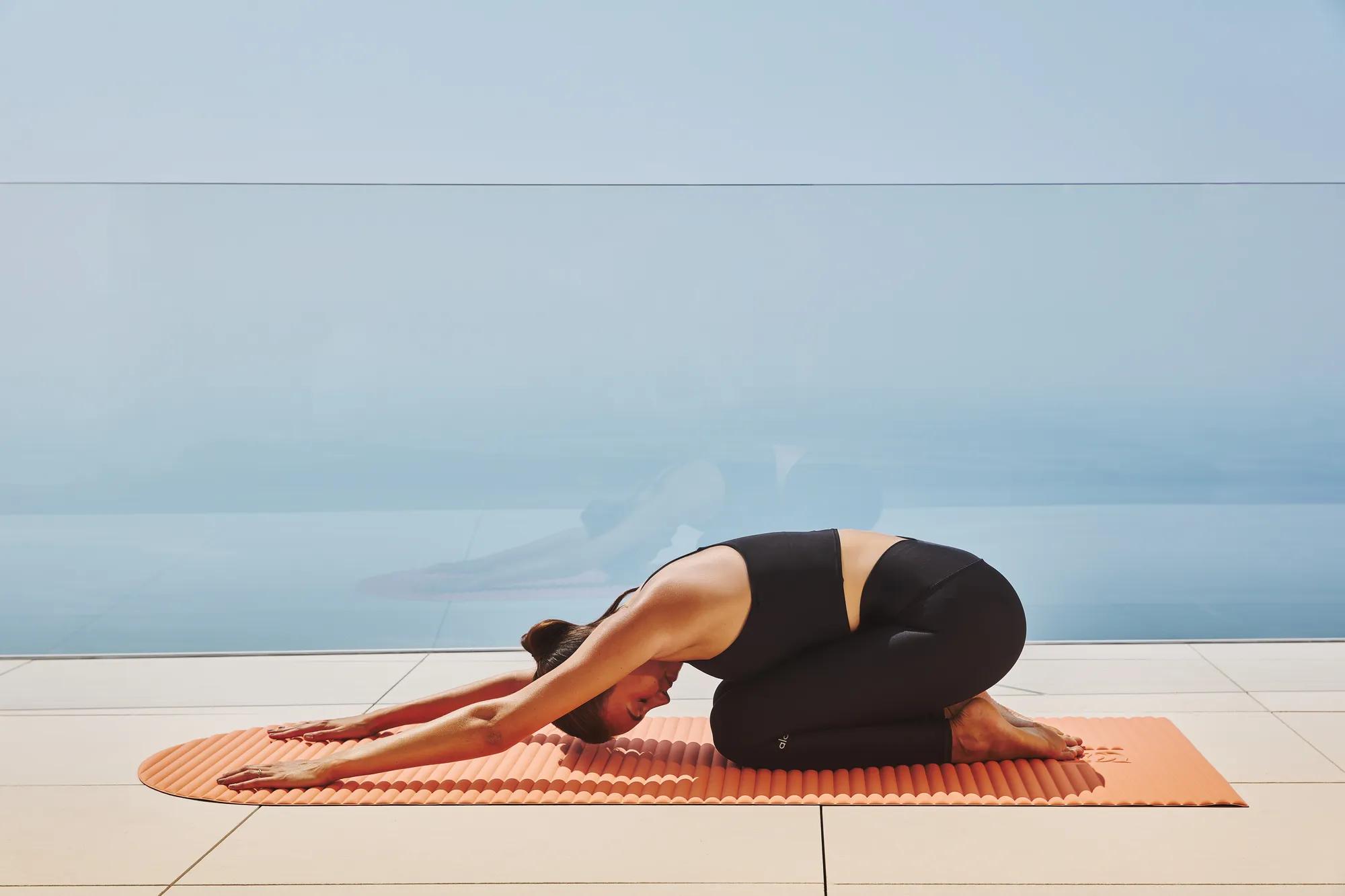 Guest practising yoga in child’s pose on a mat, with floor-to-ceiling glass overlooking the sea.
