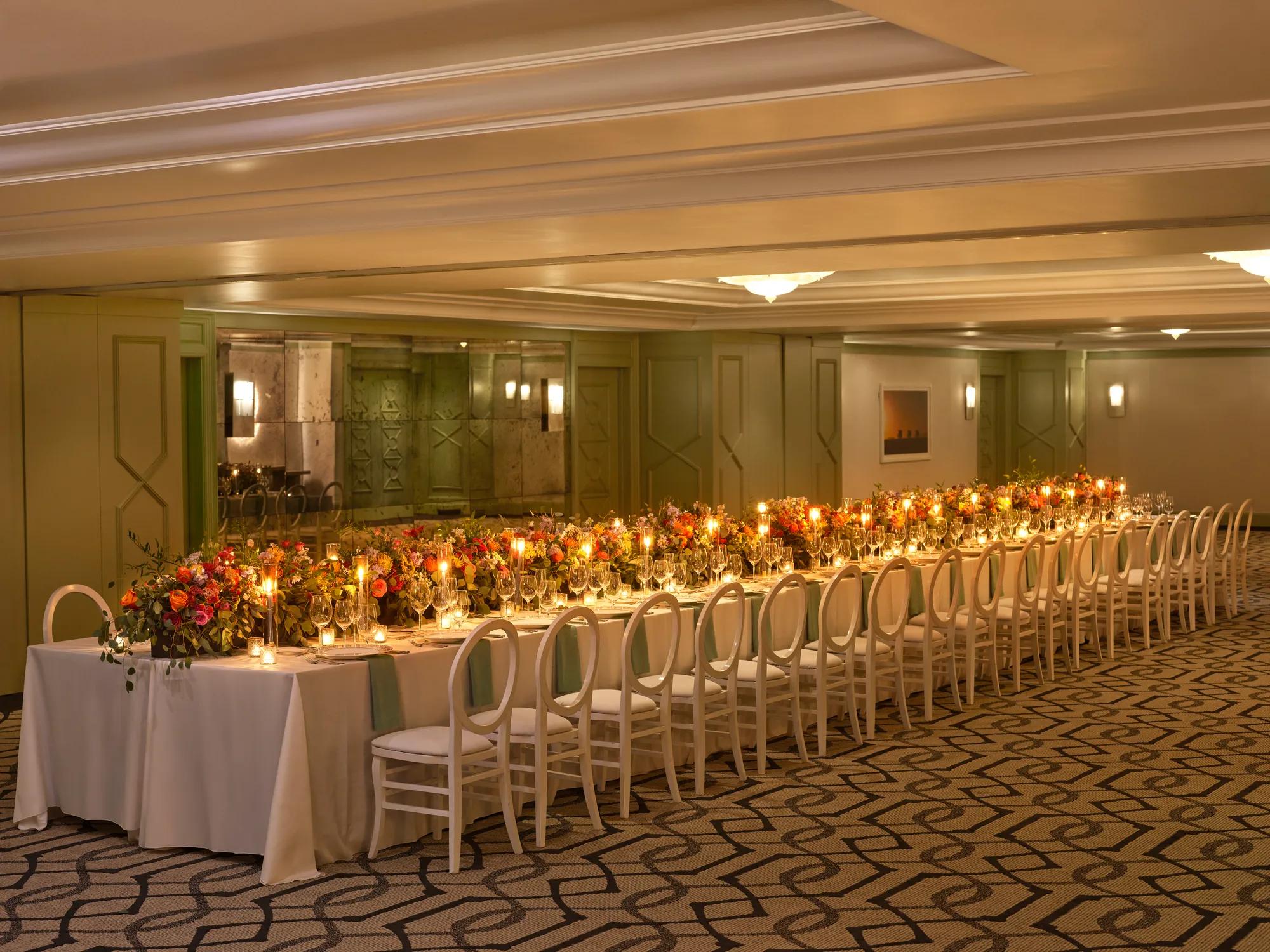 The Gallery styled for a banquet with an extra-long candlelit table, lush colorful florals, and white loop-back chairs.
