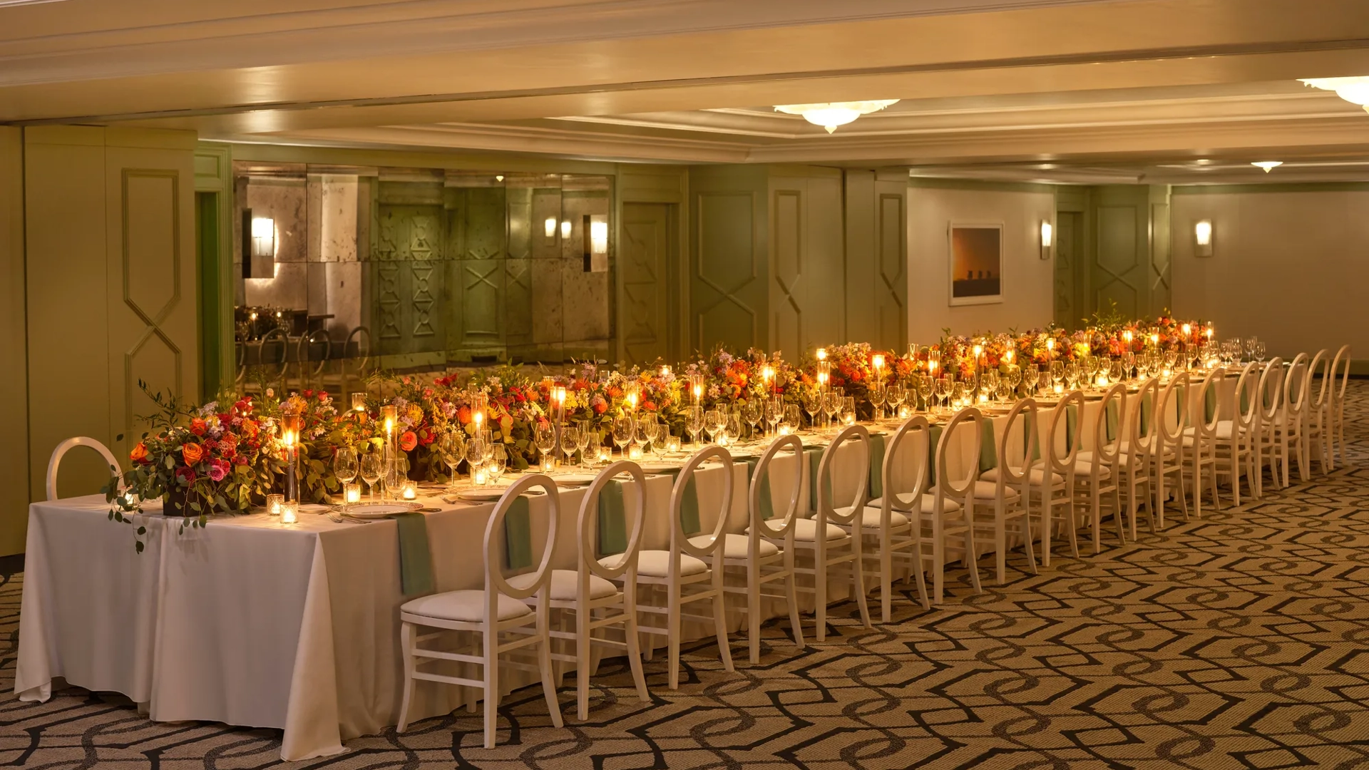 The Gallery styled for a banquet with an extra-long candlelit table, lush colorful florals, and white loop-back chairs.