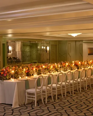 The Gallery styled for a banquet with an extra-long candlelit table, lush colorful florals, and white loop-back chairs.