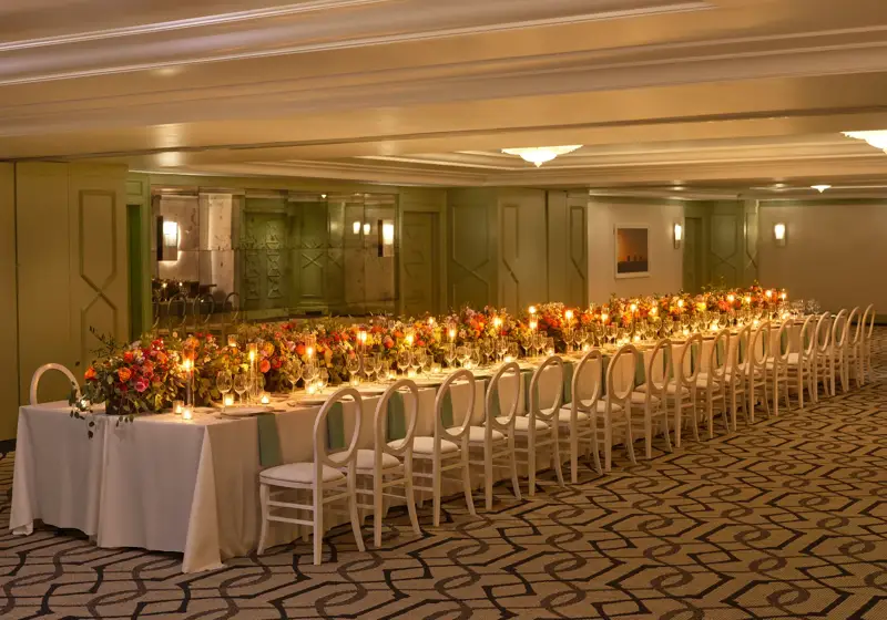 The Gallery styled for a banquet with an extra-long candlelit table, lush colorful florals, and white loop-back chairs.