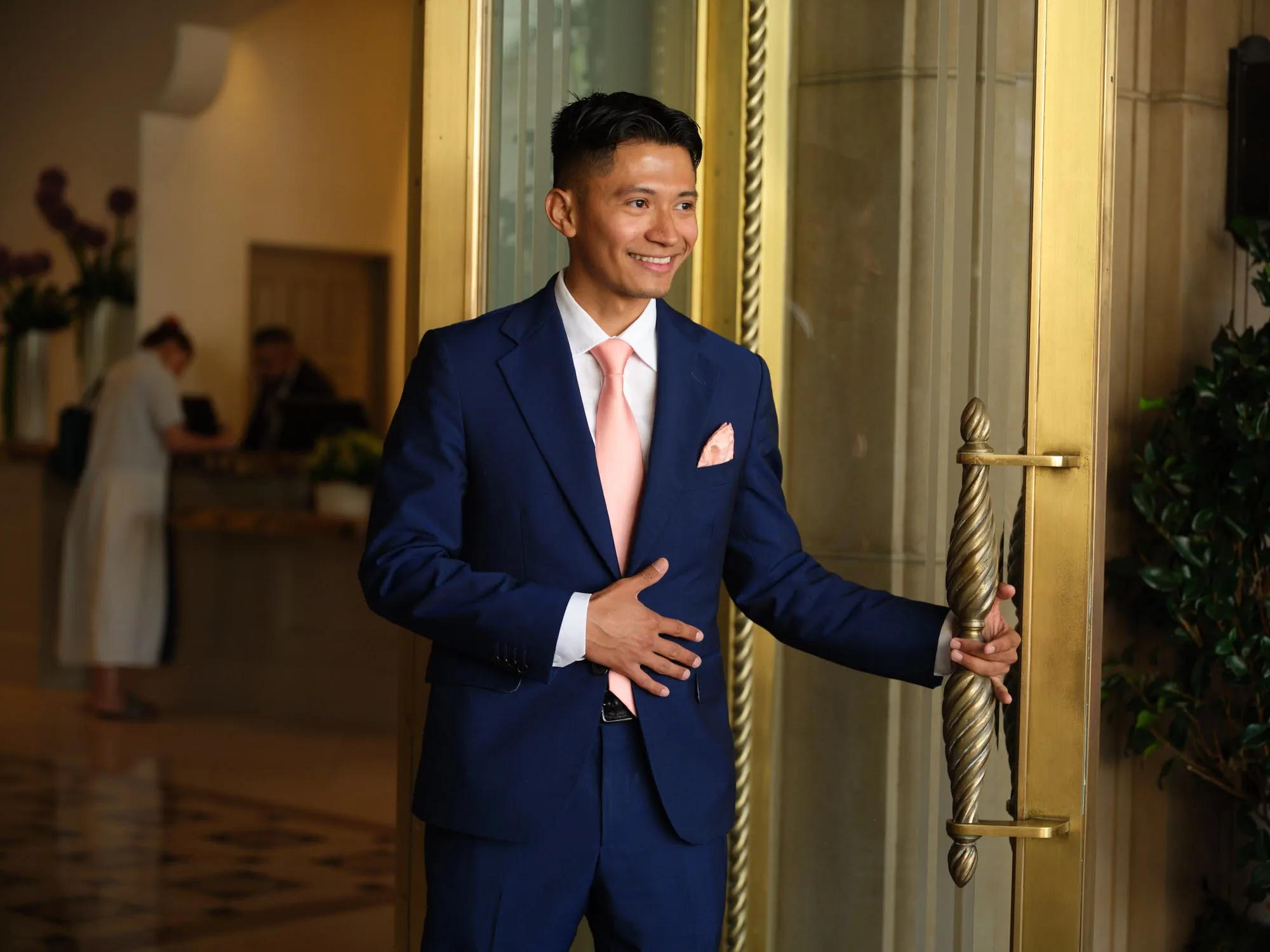 Hotel staff member in a navy suit opens an ornate gold door at a luxury Beverly Hills hotel entrance.
