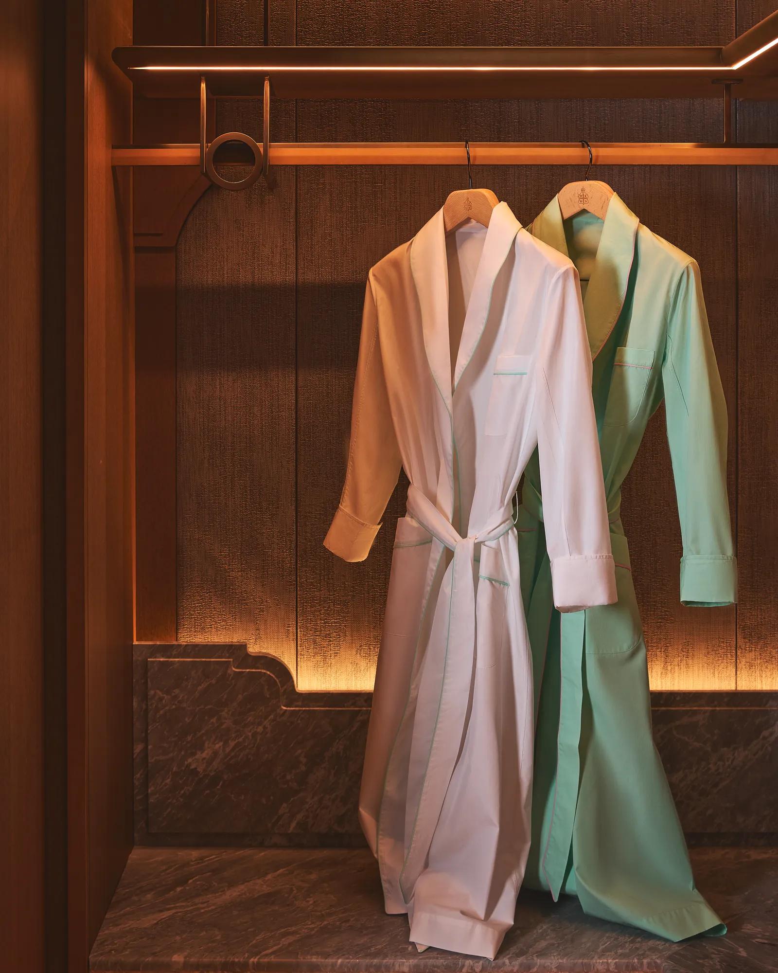 Two bathrobes hanging in a warm wooden wardrobe.