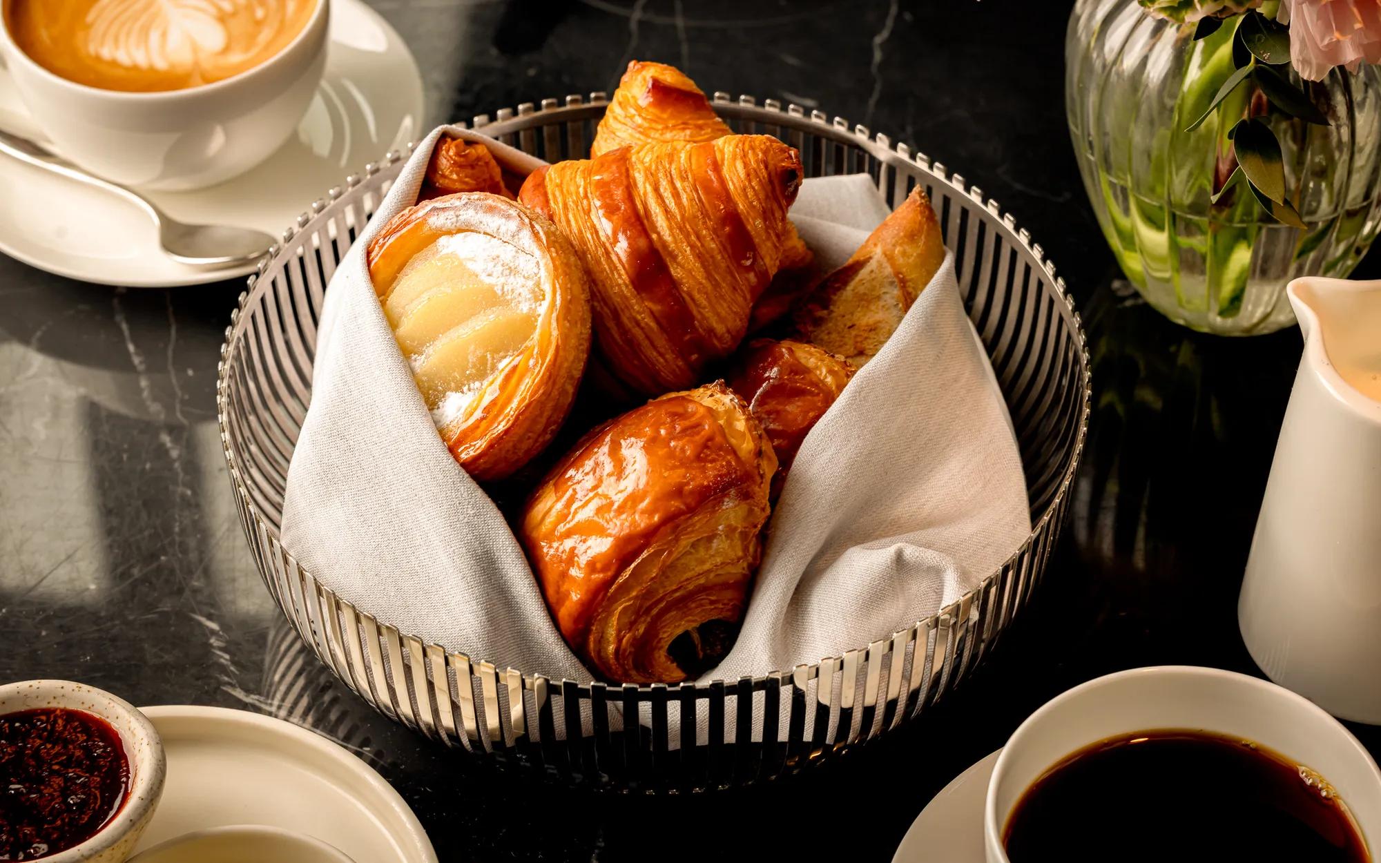 Wicker basket holding a variety of pastries, including croissants and rolls, placed on a tabletop.
