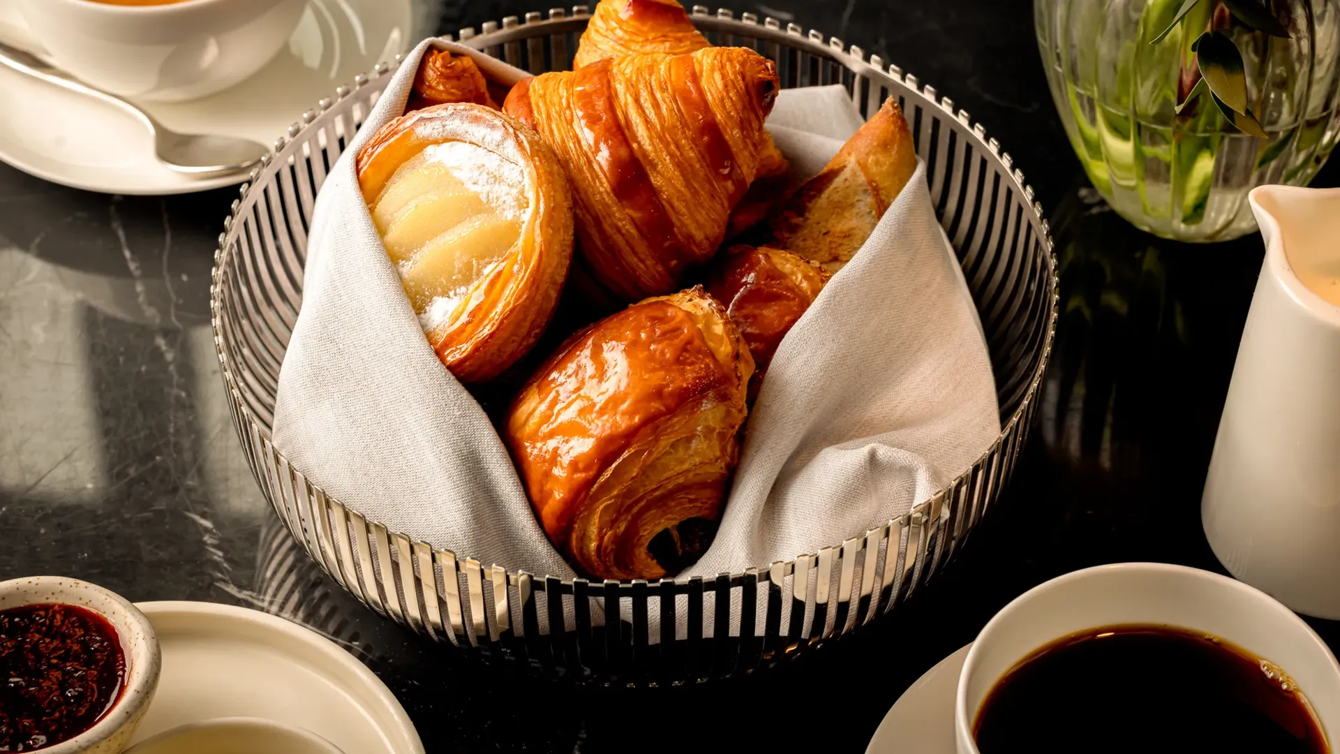 Wicker basket holding a variety of pastries, including croissants and rolls, placed on a tabletop.