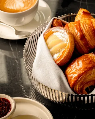 Wicker basket holding a variety of pastries, including croissants and rolls, placed on a tabletop.