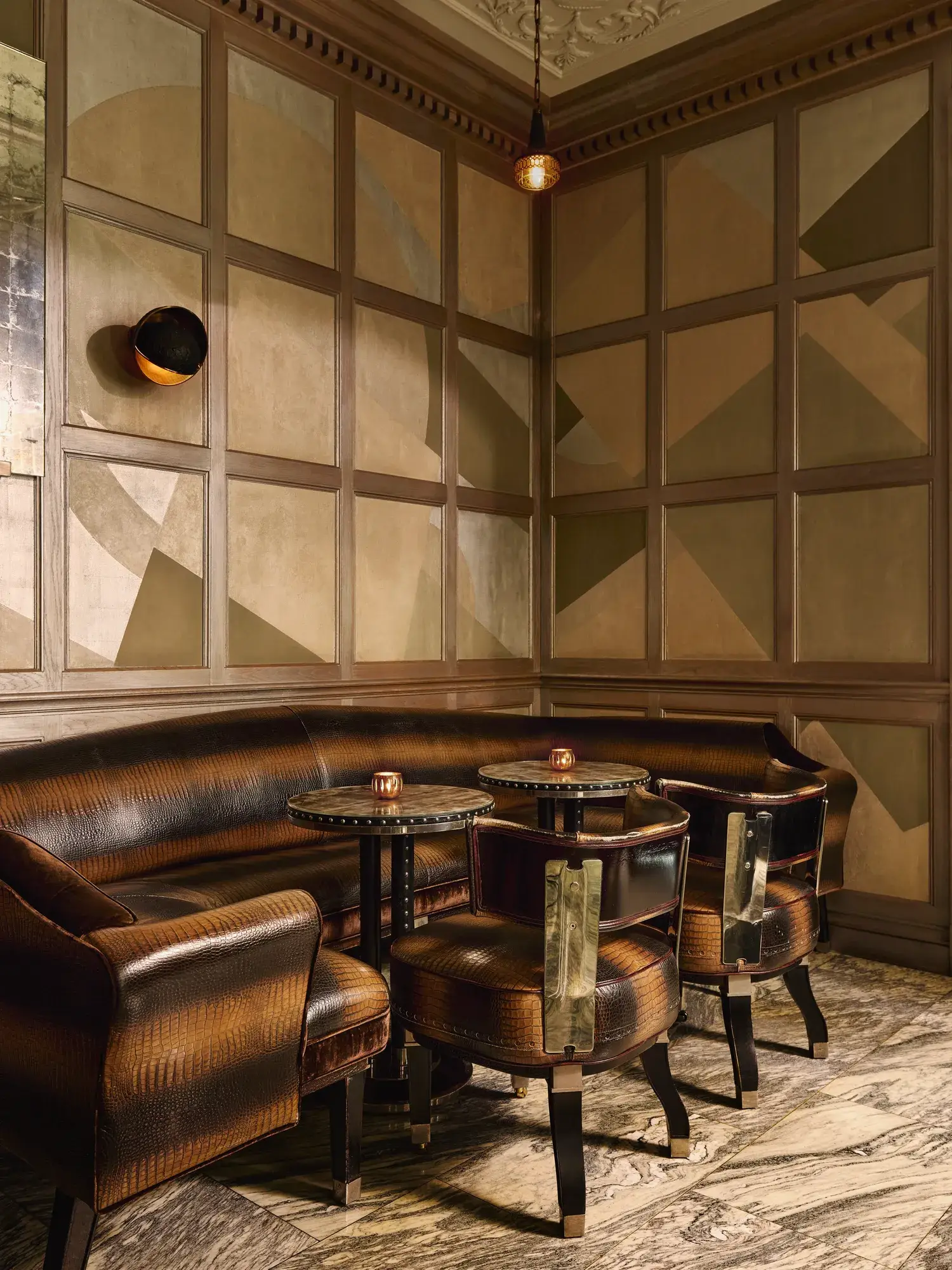 A cosy corner with curved leather banquette seating, small round tables, and geometric paneled walls in warm tones.