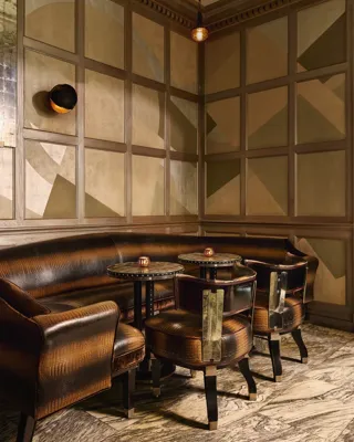 A cosy corner with curved leather banquette seating, small round tables, and geometric paneled walls in warm tones.