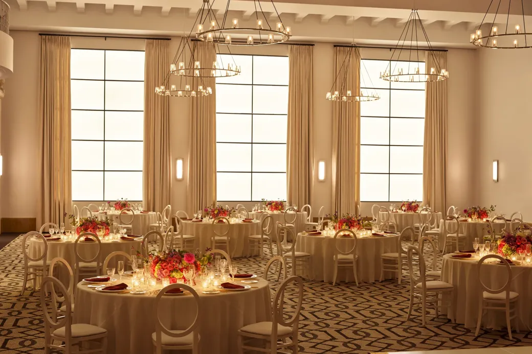 Beverly Hills Ballroom set for dinner with candlelit round tables, white chairs, and bright floral centerpieces beneath ring chandeliers.
