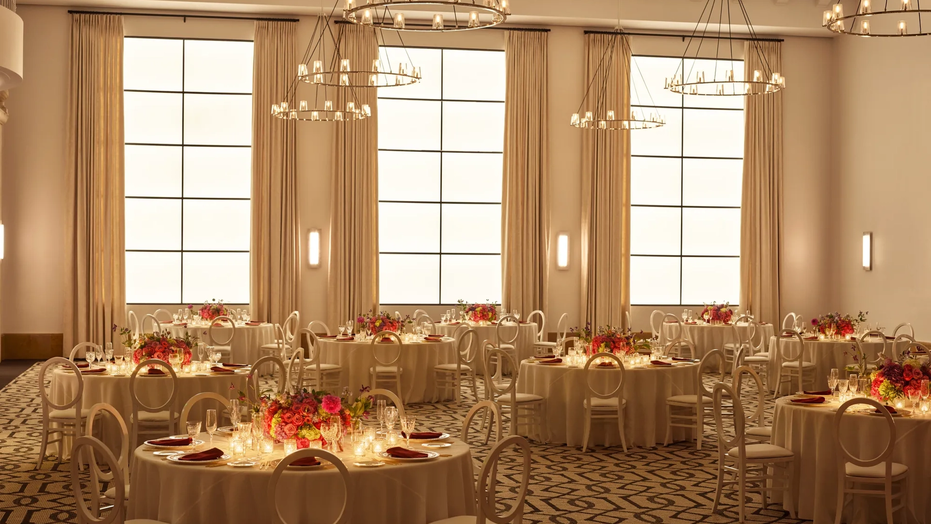 Beverly Hills Ballroom set for dinner with candlelit round tables, white chairs, and bright floral centerpieces beneath ring chandeliers.