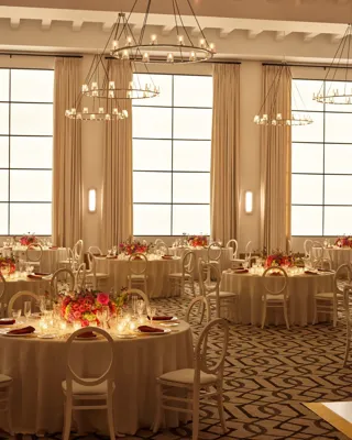 Beverly Hills Ballroom set for dinner with candlelit round tables, white chairs, and bright floral centerpieces beneath ring chandeliers.
