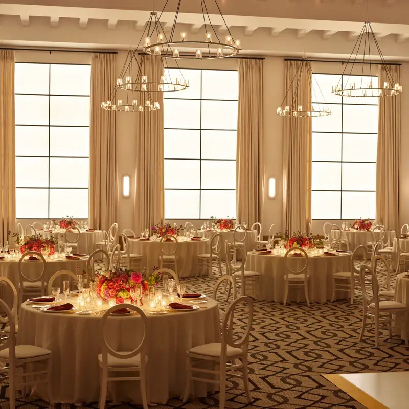 Beverly Hills Ballroom set for dinner with candlelit round tables, white chairs, and bright floral centerpieces beneath ring chandeliers.